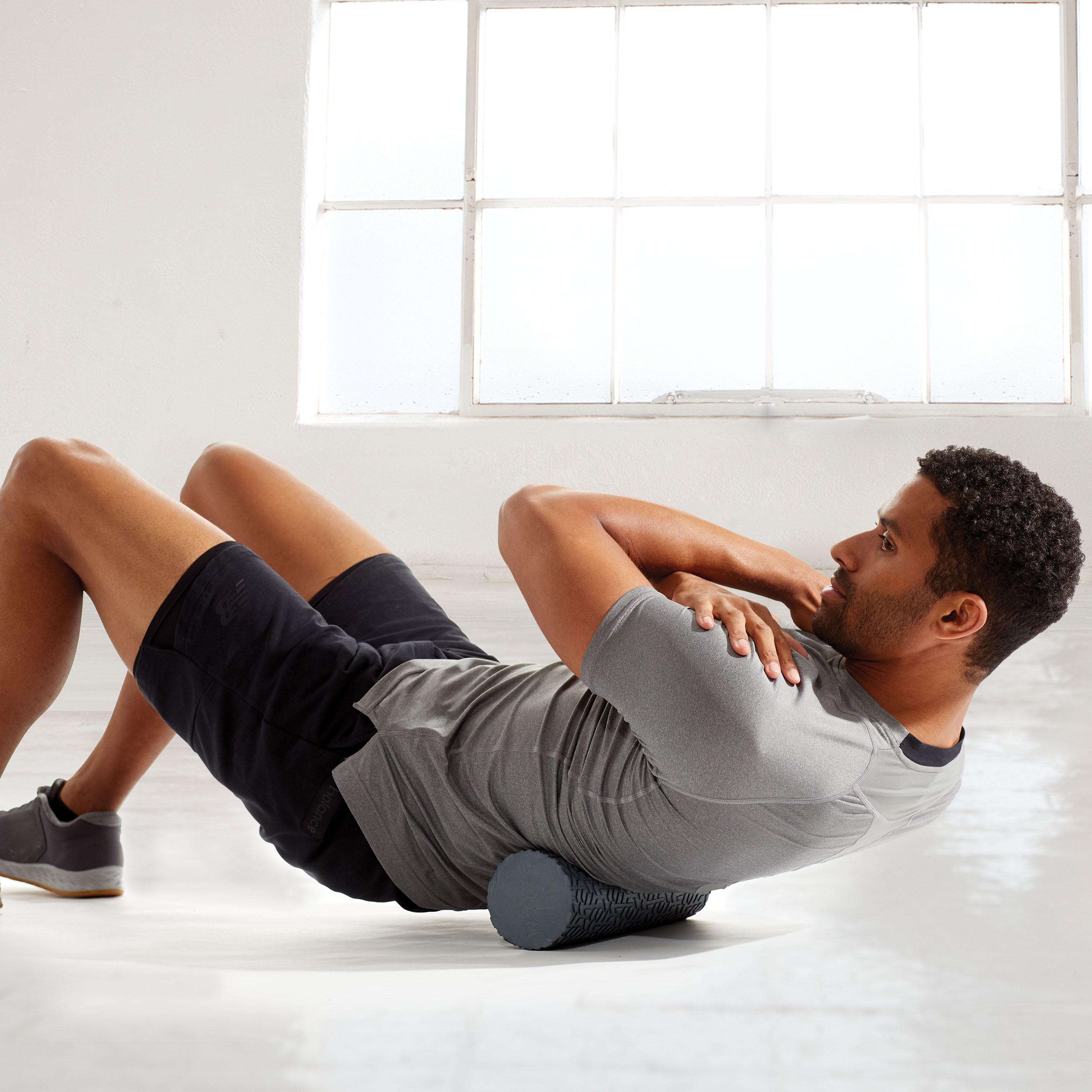 Person on ground with Restore Compact Textured Foam Roller under lower back to help massage 